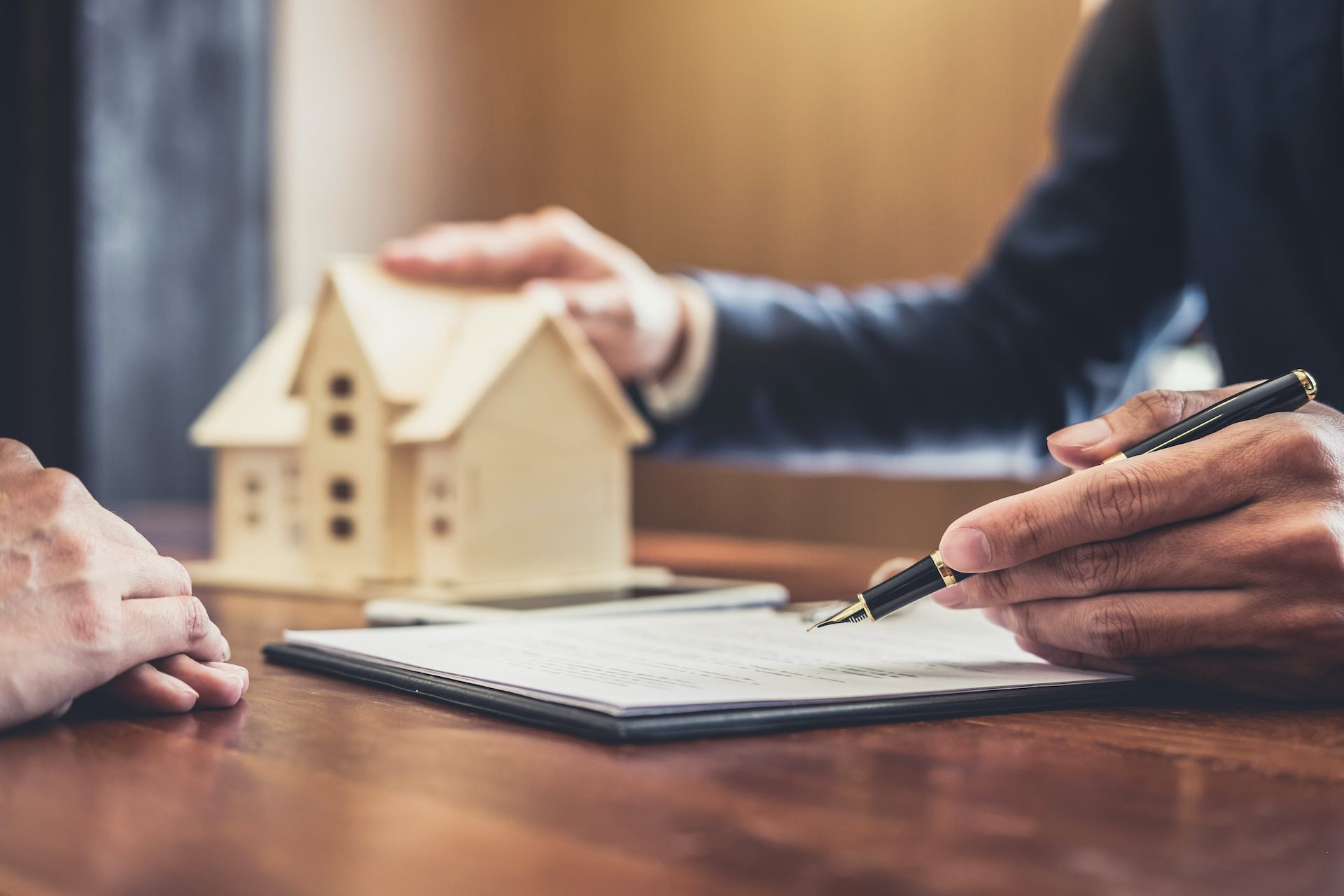 Insurance agent going over weekend and vacation rental insurance document with client with hand on model home